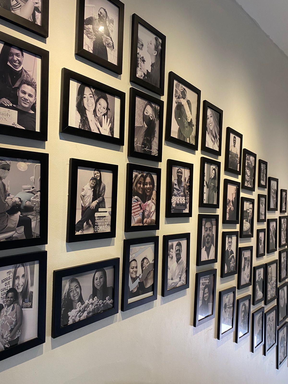 Parede com fotos de pacientes sorrindo na Clínica Odontológica Dents